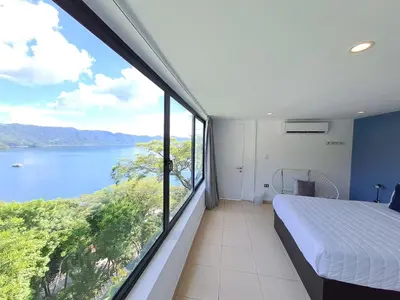 a bedroom with a large window with a view of a lake at Cardedeu Hotel Lago de Coatepeque in El Congo