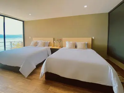 two beds in a hotel room with a large window at Cardedeu Hotel Lago de Coatepeque in El Congo