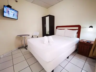 a bedroom with a large white bed with a tv on the wall at Hotel Armonía Hostal in San Salvador