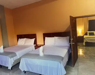 a bedroom with two beds with white sheets and a mirror at Hotel y Restaurante La Perla, Cacaopera, Morazan, El Salvador in Cacaopera