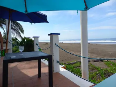 a table with a wine glass and an umbrella on the beach at MARDEORO BEACH HOUSE in Barra de Santiago