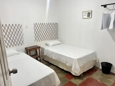 two beds in a small room with white sheets at Hostal Villa Marta in Santa Ana