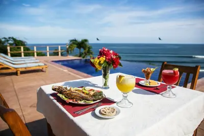 a table with a plate of food and a view of the ocean at Hotel Los Mangos El Salvador in El Cuco