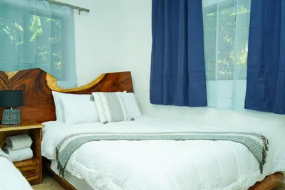 two beds in a bedroom with blue curtains at Buena Vista El Zonte in El Zonte