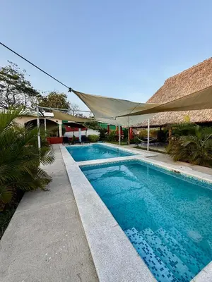 a swimming pool next to a building with a tent at Lomeli’s Home, 5 minutos del Tunco in La Libertad