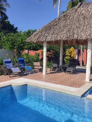 a swimming pool with chairs and a thatch roof at Rancho Del Oso Tuerto in Marcelino