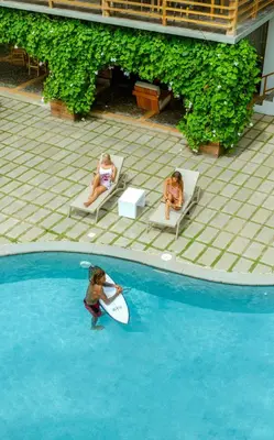 two women sitting in chairs with a surfboard in a swimming pool at Mirasurf Hotel & Waves in El Sunzal