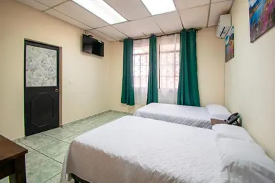 two beds in a room with green curtains and a window at Lorenzo Hotel in San Salvador