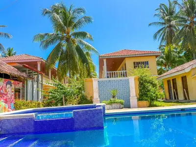a swimming pool in front of a house with palm trees at Hotel y Restaurante Punta Diamantes in Acajutla