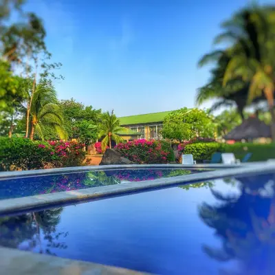 a swimming pool with flowers and a house in the background at Puerto Barillas in Bahia de Jiquilisco