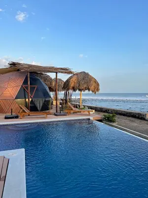 a swimming pool with umbrellas and the ocean at Almare Zonte - BeachFront Glamping Hotel in El Zonte