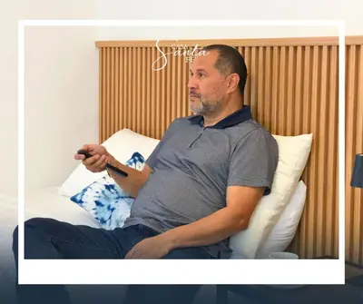 a man sitting on a bed holding a remote control at Casa Santa Fe in San Salvador