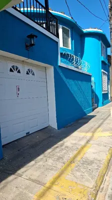 a blue house with a white garage door and a balcony at Hostal Primaveras nest habitación 3 in Santa Ana