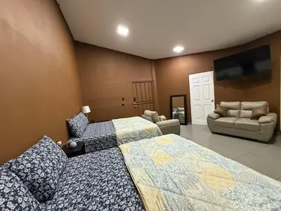 a bedroom with two beds and two chairs and a flat screen tv at El Mangal 2 B&B in Suchitoto