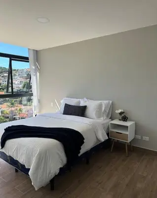 a white bedroom with a large bed and a window at Cielito Lindo, vista espectacular en 11 nivel in Antiguo Cuscatlán