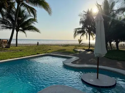 a swimming pool with an umbrella next to the beach at Villa San Juan, playa Costa Azul in Acajutla