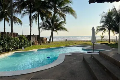 a swimming pool next to a beach with palm trees at Villa San Juan, playa Costa Azul in Acajutla