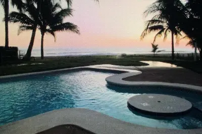 a swimming pool next to the ocean with palm trees at Villa San Juan, playa Costa Azul in Acajutla