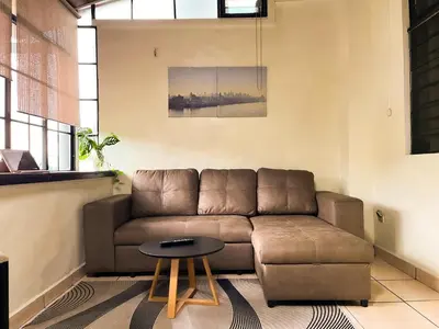a living room with a brown couch and a table at Apartamento dos habitaciones baños completos WiFi y AC todo el apto, parqueo interno,San Salvador, Colonia escalón in San Salvador
