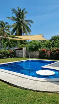 a blue swimming pool with a tan umbrella over it at Casa con Piscina y Rancho, cerca de Estero y Playa in El Zapote
