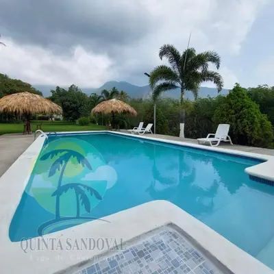 a blue swimming pool with two chairs and palm trees at Quinta Sandoval Lago de Coatepeque in Santa Ana