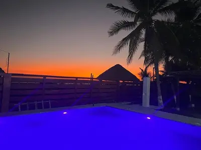 a blue pool with a palm tree and a sunset at Rancho El Angel, La Costa Del Sol in San Luis La Herradura