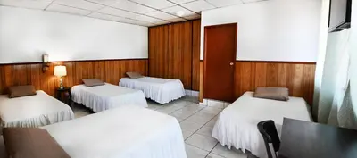 a room with three beds and a table in it at Hotel Manantiales El Salvador in San Salvador