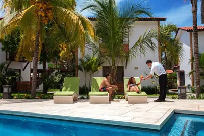 a man standing next to two people sitting in chairs by a pool at Boca Olas Resort Villas in La Libertad