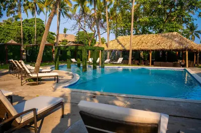 a swimming pool with chairs and a thatch roof at Eco Suites El Zonte in La Libertad