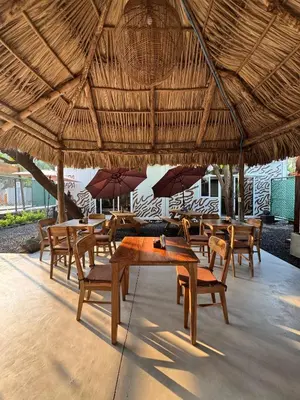 a group of tables and chairs under a straw umbrella at Eco Suites El Zonte in La Libertad