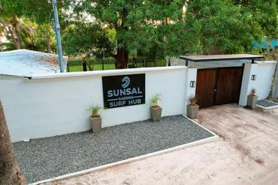a sign on a white wall with plants next to a gate at SunSal Garden Surf Hub in El Sunzal