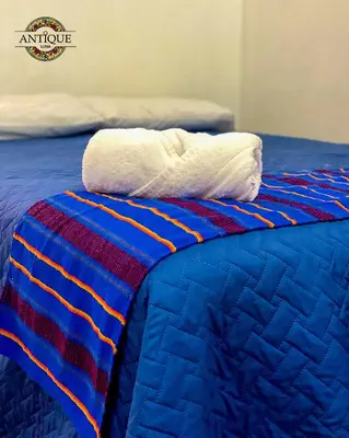 a bed with a blue and red quilt and two towels at Hostal Antique Luna in Santa Ana