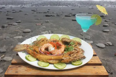 a plate of shrimp and a drink on the beach at Punta Roca Surf Resort in La Libertad