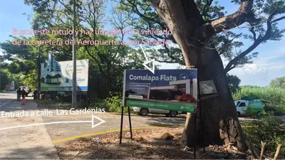 a sign in front of a tree next to a street at Stay with us just 5 minutes from the international airport of El Salvador in Las Flores