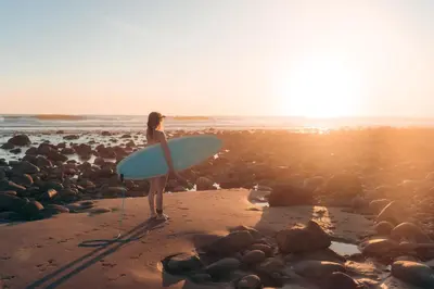 a woman standing on a beach holding a surfboard at Casa de Mar Hotel And Villas in La Libertad