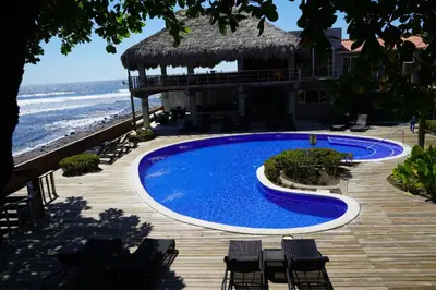 a swimming pool next to a building with the ocean at Casa de Mar Hotel And Villas in La Libertad