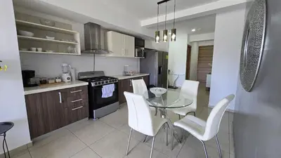 a kitchen with a glass table and white chairs at Acogedor y Centrico Apartamento in San Salvador