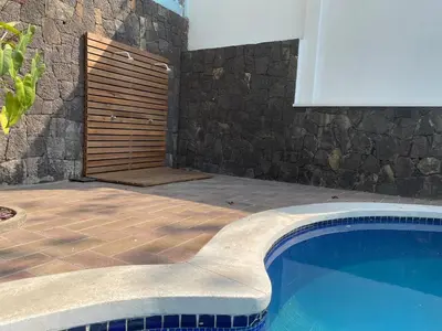 a swimming pool next to a stone wall with a wooden door at Casa Tropical Kaylani in Tamanique