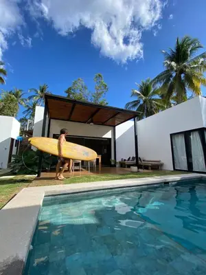 a man holding a surfboard next to a swimming pool at Villa Uma 50m to Zonte wave 2Bdr in El Zonte