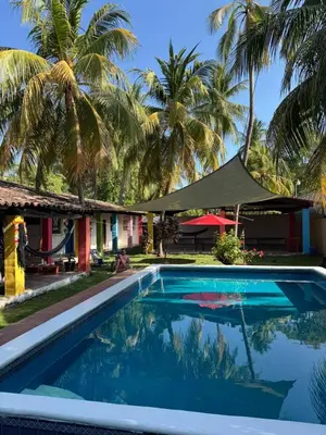 a swimming pool in front of a house with palm trees at Rancho Samba do Sol in Acajutla
