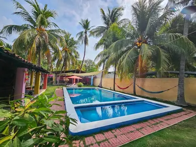 a swimming pool in front of a house with palm trees at Rancho Samba do Sol in Acajutla