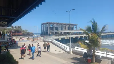 a group of people walking on a pier next to the ocean at via costera 1 in La Libertad
