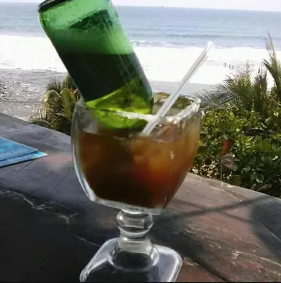 a drink in a glass on a table with the beach at Hotel Casa Miramar in Tamanique