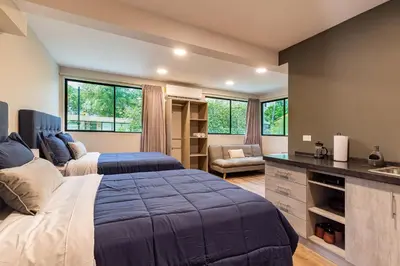 a bedroom with two beds and a kitchen with windows at Lora Loca Inn in El Zonte