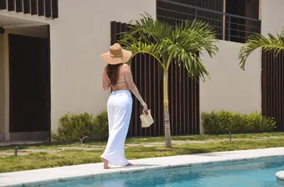 a woman in a hat standing next to a swimming pool at Astra Beach Club & Resort in Marcelino