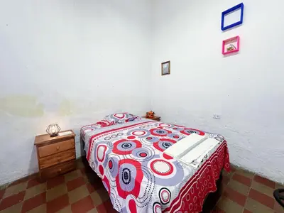 a bedroom with a bed with a red and white comforter at Hostal Los Milagros in Santa Ana