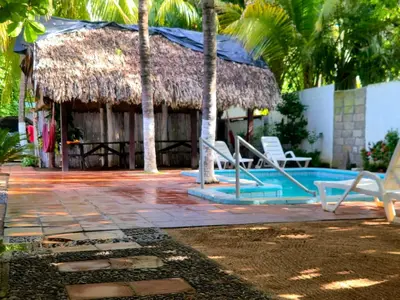 a resort with a swimming pool and a straw hut at Hotel y Restaurante Los Cobanos Village Lodge in Los Cóbanos