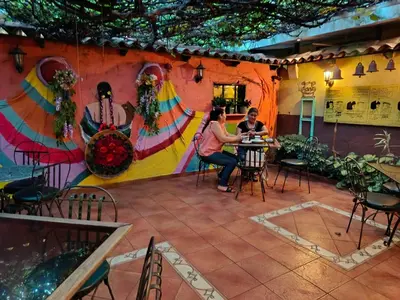 two people sitting at a table in front of a wall with a mural at Expresión cultural restaurante y alojamiento in Santa Ana
