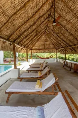a row of lounge chairs under a straw roof at Las Golondrinas El Zonte, El Salvador in El Zonte