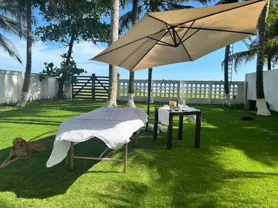 a dog laying on the grass next to a table and an umbrella at Oceanfront Solar Paradise-Steps to the Sea in El Zapote